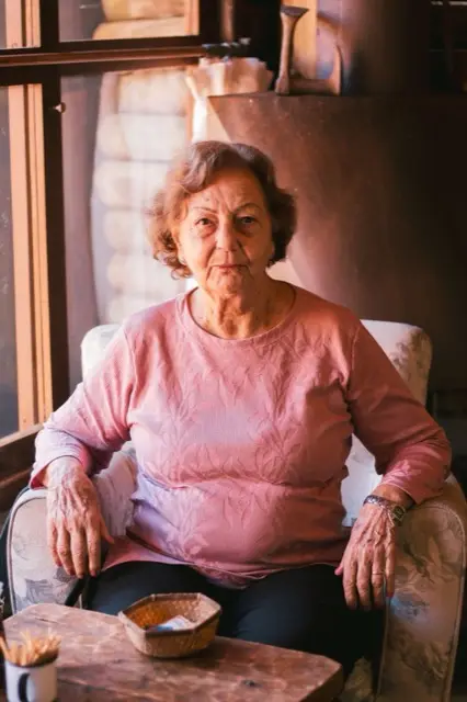 Mujer mayor mirando por la ventana, reflexionando sobre el futuro de su familia